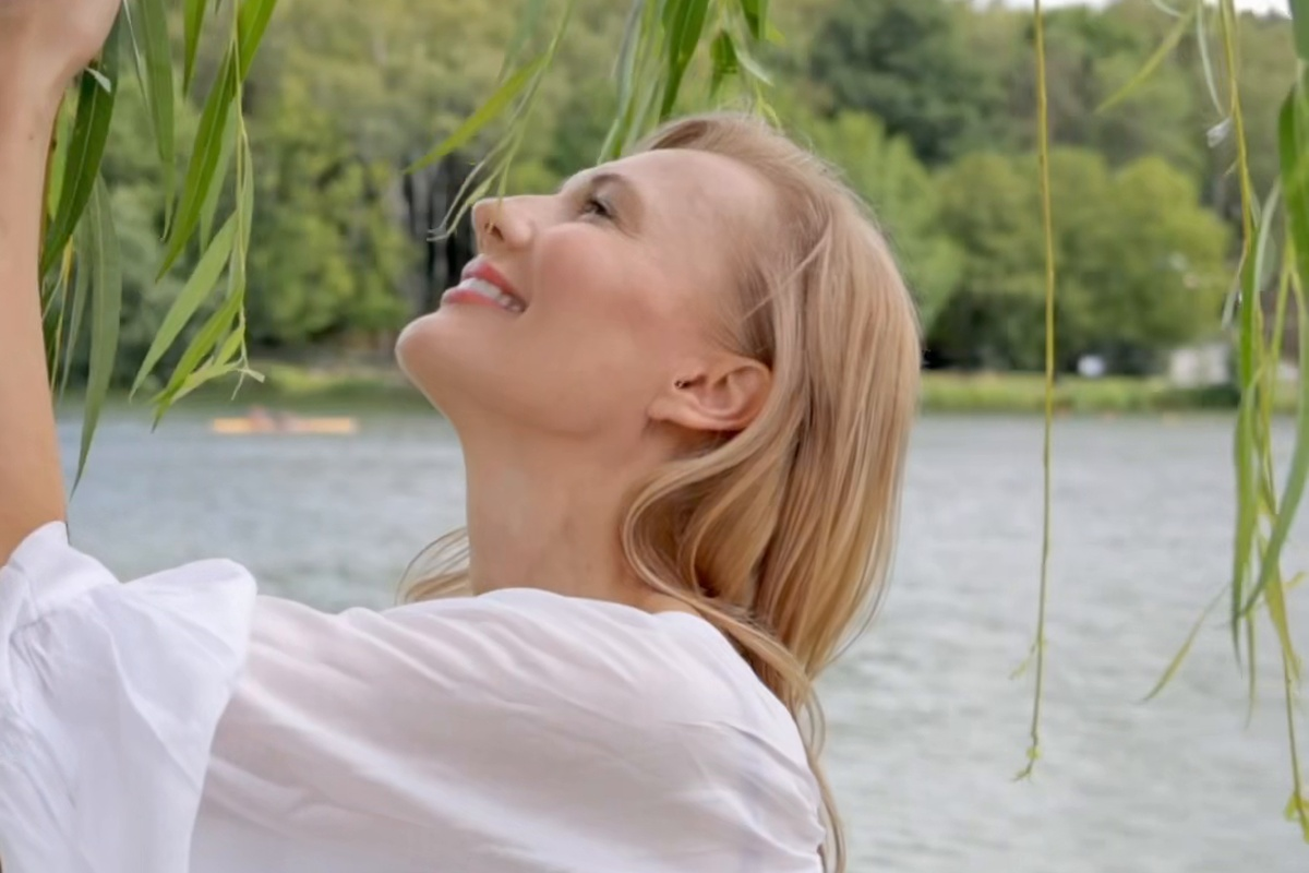 Iwona Kubisiak pod wierzbą nad jeziorem, z twarzą uniesioną do światła