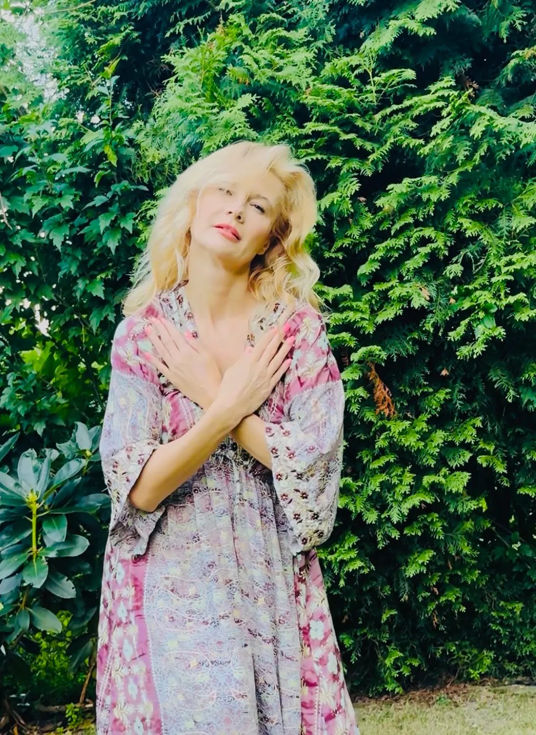 Iwona Kubisiak w ogrodzie z dłońmi skrzyżowanymi na klatce piersiowej - gest kontaktu ze sobą